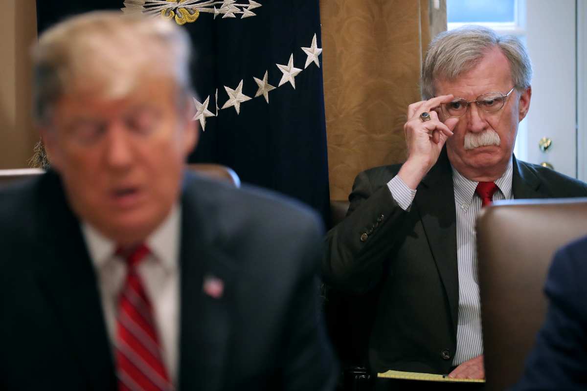 John Bolton (R) listens to U.S. President Donald Trump talk to reporters during a meeting of his cabinet in the Cabinet Room at the White House. Image Source: Getty Images | Photo by Chip Somodevilla